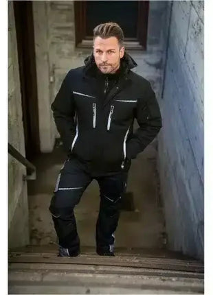 Mann in schwarzer Arbeitsjacke und Hose mit Reflektoren, steht auf Treppe im Außenbereich
