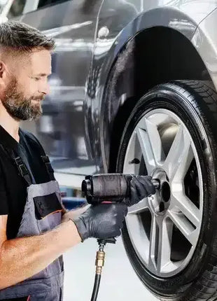 Mechaniker montiert Autoreifen mit Schlagschrauber, trägt schwarze Schutzhandschuhe, Werkstatt