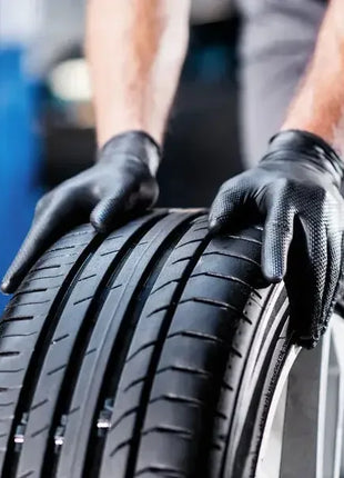 Mechaniker mit schwarzen Einweghandschuhen montiert Autoreifen, Werkstatt Hygiene