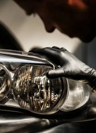 Mann mit schwarzen Schutzhandschuhen reinigt Autoscheinwerfer, Hygiene und Arbeitsschutz
