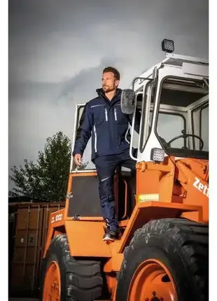 Mann in Arbeitskleidung steht auf orangefarbenem Bagger, Outdoor Industrieszene