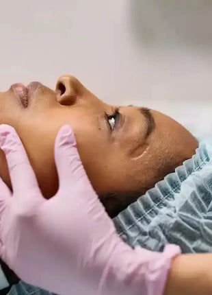Kosmetische Behandlung mit rosa Einweghandschuhen, Patientin mit Haube in Praxis