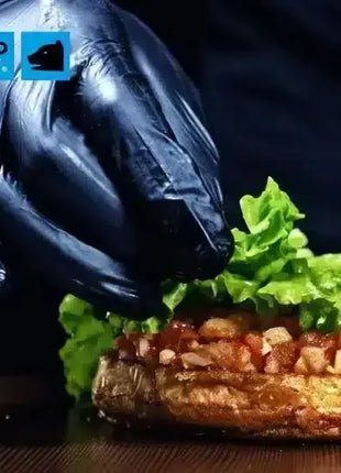 Hand mit schwarzem Einweghandschuh bereitet Burger mit Salat hygienisch zu, Lebensmittelhygiene