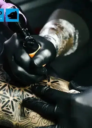 Tattoo-Künstler mit schwarzen Handschuhen sticht geometrisches Tattoo auf Unterarm, Hygiene wichtig