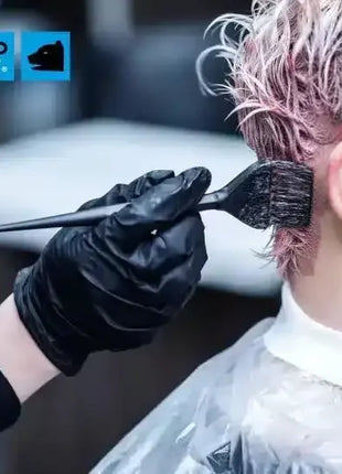 Friseur trägt Haarfarbe mit Pinsel auf kurzes Haar, schwarze Einweghandschuhe, Hygieneschutz