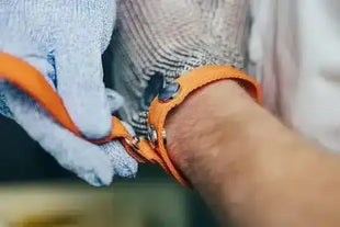Person legt schnittfeste Sicherheitshandschuhe mit orangefarbenem Handgelenksband an