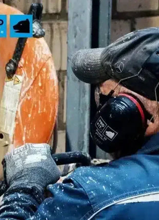 Arbeiter mit Gehörschutz, Schutzbekleidung und Handschuhen bedient Trennschleifer auf Baustelle