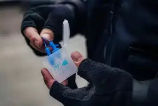 Person hält Spenderbox mit blauen Einweghandschuhen, Outdoor-Handschuhe sichtbar