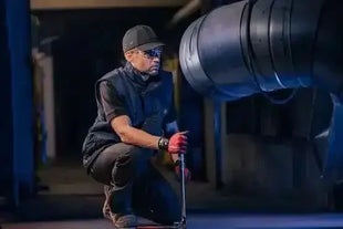 Werkstattmitarbeiter mit Schutzkleidung prüft industrielle Lüftungsanlage in dunkler Halle