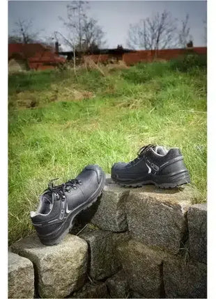 Schwarze Arbeitsschuhe mit Sicherheitskappe auf Steinmauer im Freien, Schutzschuhe