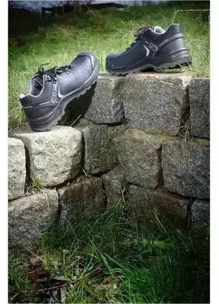 Schwarze Sicherheitsschuhe mit rutschfester Sohle auf Natursteinen im Außenbereich