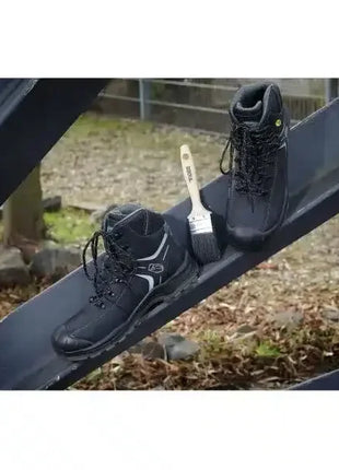 Schwarze Sicherheitsschuhe mit Pinsel auf Metallträger, Outdoor-Arbeitsumgebung