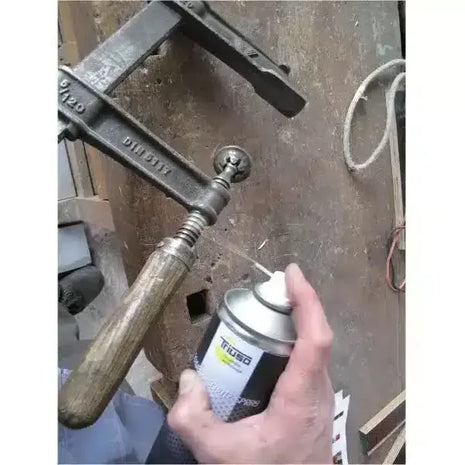 Schmiermittelspray wird auf Metall-Schraubzwinge in Werkstattumgebung aufgetragen