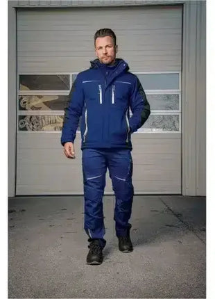 Mann in blauer, wetterfester Arbeitskleidung mit Schutzjacke und Hose steht vor Garagentor