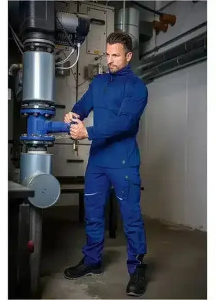 Mann in blauer Arbeitskleidung dreht ein Ventil in Technikraum, PSA, Industriearbeitsplatz