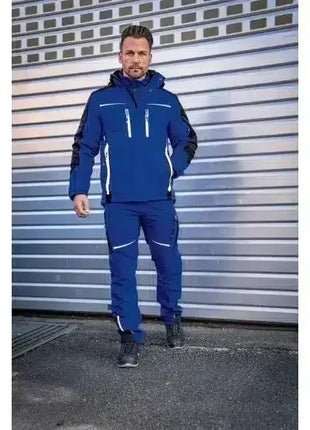 Mann in blauer Arbeitskleidung mit Jacke und Hose, stehend vor Industrie-Rolltor, Berufsbekleidung
