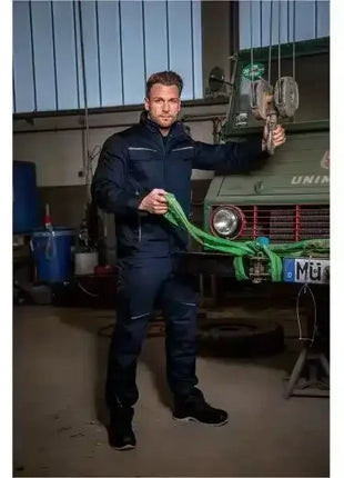 Mann in Arbeitskleidung in Werkstatt neben Unimog, hält grünes Abschleppseil, professionelle Hygiene