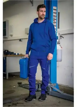 Mann in blauer Arbeitskleidung mit Kanister in moderner Werkstatt, professionelle Hygienebekleidung