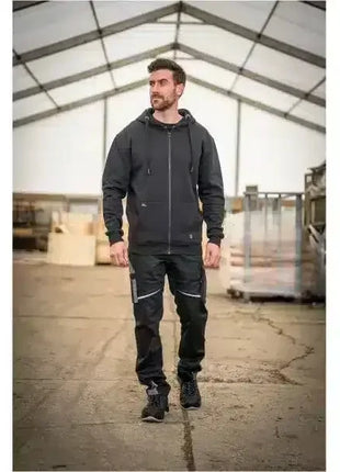 Mann in schwarzer Arbeitskleidung mit Kapuzenjacke und Arbeitshose in Industriehalle