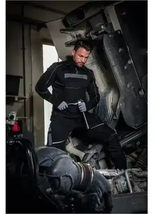 Mechaniker in schwarzer Arbeitskleidung bei LKW-Reparatur, professionelle Werkstatt, PSA