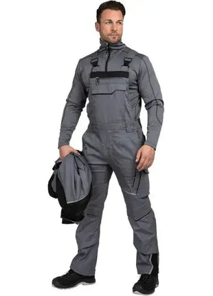 Mann in grauer Arbeitslatzhose, Funktionsjacke in der Hand, professionelle Arbeitskleidung