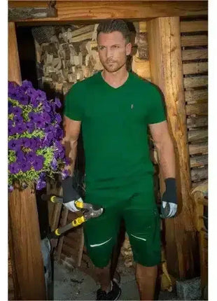Mann in grüner Arbeitskleidung mit Astschere und Handschuhen vor Holzlager, Gartenarbeit Szene