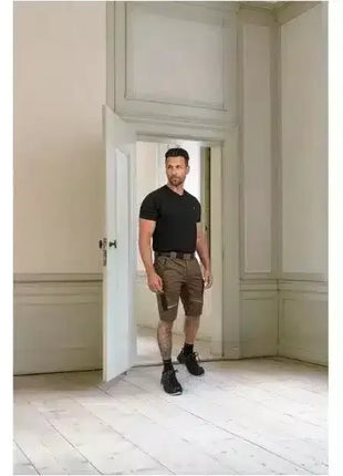 Mann in schwarzem Shirt und brauner Arbeitsshorts, steht in hellem Raum, robuste Berufskleidung