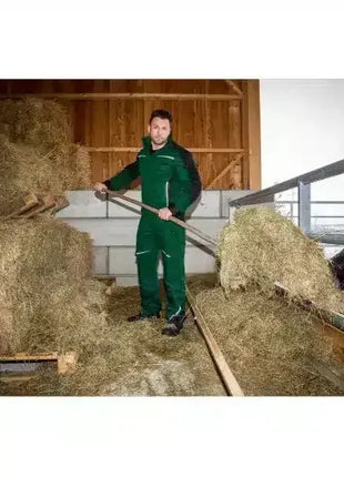 Landwirt in grüner Arbeitskleidung verteilt Heu im Stall, professionelle Hygieneumgebung