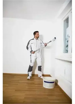 Maler in Arbeitskleidung streicht weiße Wand mit Farbrolle in hellem Raum, Hygieneprodukte