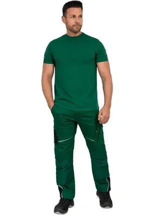Mann in grüner medizinischer Berufskleidung mit Hose und T-Shirt, stehend, neutraler Hintergrund