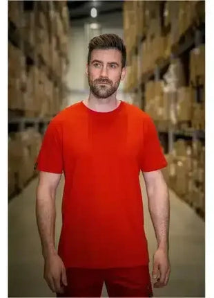 Mann in rotem T-Shirt steht im Lager vor Regalen mit Kartons, Arbeitskleidung, Logistik