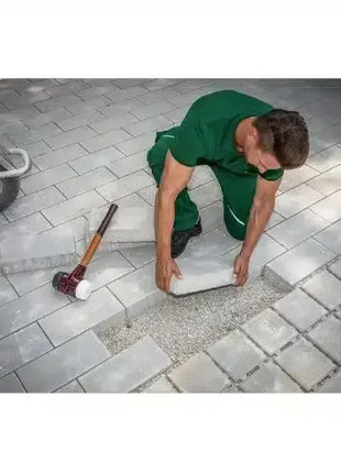 Handwerker verlegt graue Pflastersteine auf Kiesbett, Werkzeug neben Baustelle