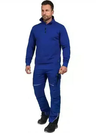 Mann in blauer Arbeitskleidung und Sicherheitsschuhen, stehend vor weißem Hintergrund.