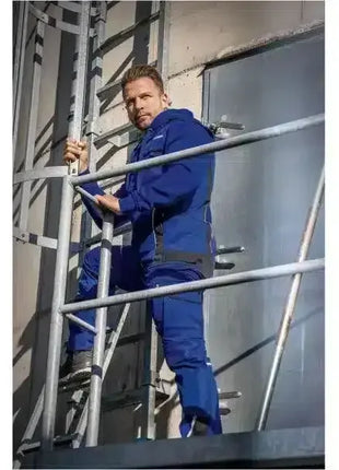 Mann in blauer Arbeitskleidung klettert Leiter an Industriegebäude, PSA Arbeitsbekleidung