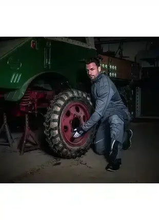 Mann im Arbeitsanzug wechselt Reifen an grünem Oldtimer-Traktor in Werkstatt, professionelle Schutzkleidung