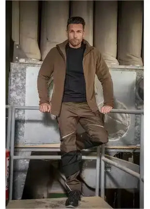 Mann in brauner Arbeitskleidung mit schwarzem Shirt und Sicherheitsschuhen, Industrieumgebung, moderne Berufsbekleidung