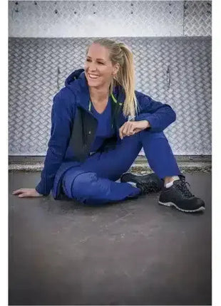 Frau in blauer medizinischer Arbeitskleidung sitzt lächelnd vor Metallwand, Hygiene Bekleidung