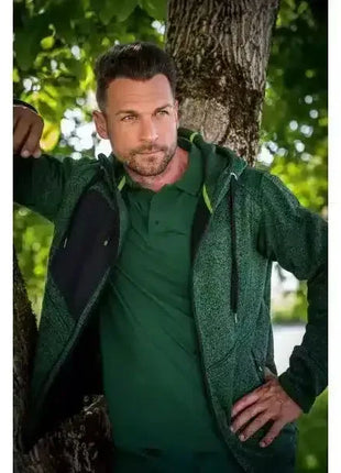 Mann mit dunkelgrüner Jacke und Poloshirt steht im Freien an einem Baum, Sommermode Herren