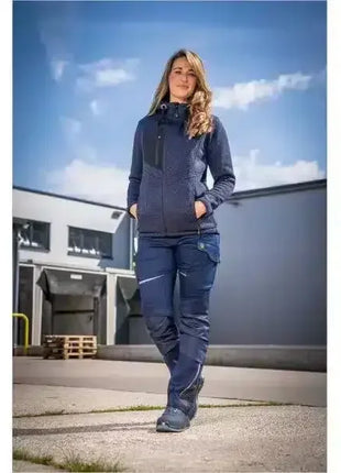Frau in blauer Arbeitskleidung steht vor Lagergebäude, professionelle Schutzkleidung