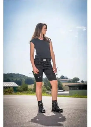 Frau trägt schwarze Arbeitsshorts und Sicherheitsschuhe im Freien, praxisorientierte Berufskleidung.