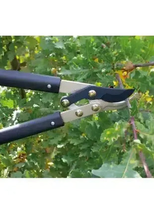 Gartenschere mit langen Griffen schneidet Ast, Nahaufnahme vor grünem Blattwerk