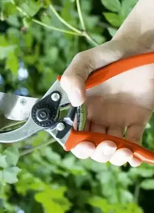 Hand hält Astschere mit rotem Griff, schneidet Ast im grünen Garten, Gartenschere Werkzeug