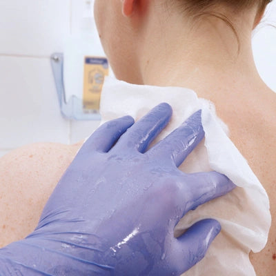 Pflegeperson mit blauen Einmalhandschuhen reinigt Rücken mit feuchtem Tuch – ideal für Inkontinenzpflege und medizinische Versorgung