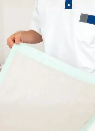Pflegekraft legt saugfähige Einweg-Bettschutzeinlage auf Bett, Hygieneartikel im Hintergrund