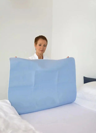 Pflegekraft legt saugfähige Inkontinenzunterlage auf ein Bett, Hygieneprodukt im Einsatz