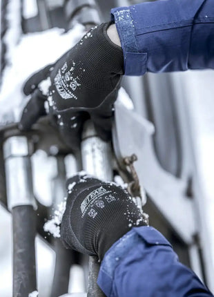 Arbeiter mit schwarzen NITRAS Schutzhandschuhen arbeitet an Metallrohren im Schnee, Arbeitsschutz Winter
