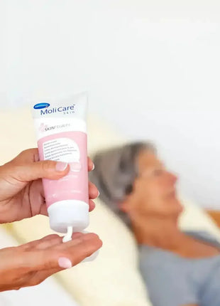 Pflegekraft trägt MoliCare Skin Hautschutzcreme auf, ältere Person im Pflegebett, medizinische Hautpflege
