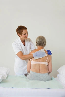 Pflegekraft wendet Wärmekompresse auf Rücken einer älteren Patientin an – professionelle Pflege bei Inkontinenz & medizinischen Bedürfnissen